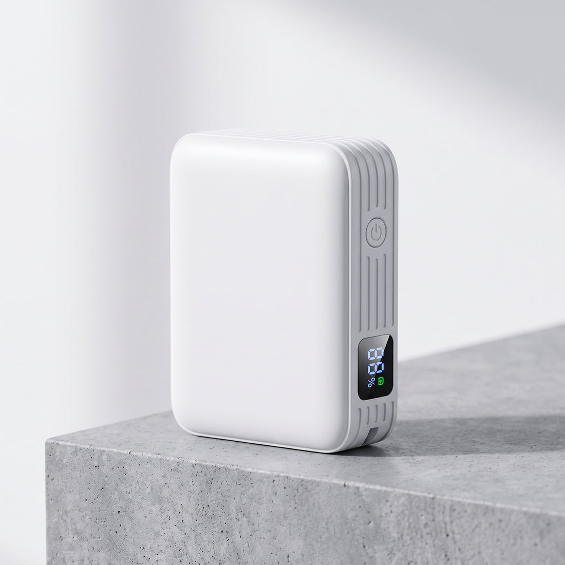 A white rectangular portable power bank with a small digital display and vertical ribbed side detail, standing on a gray concrete surface against a light gray background.