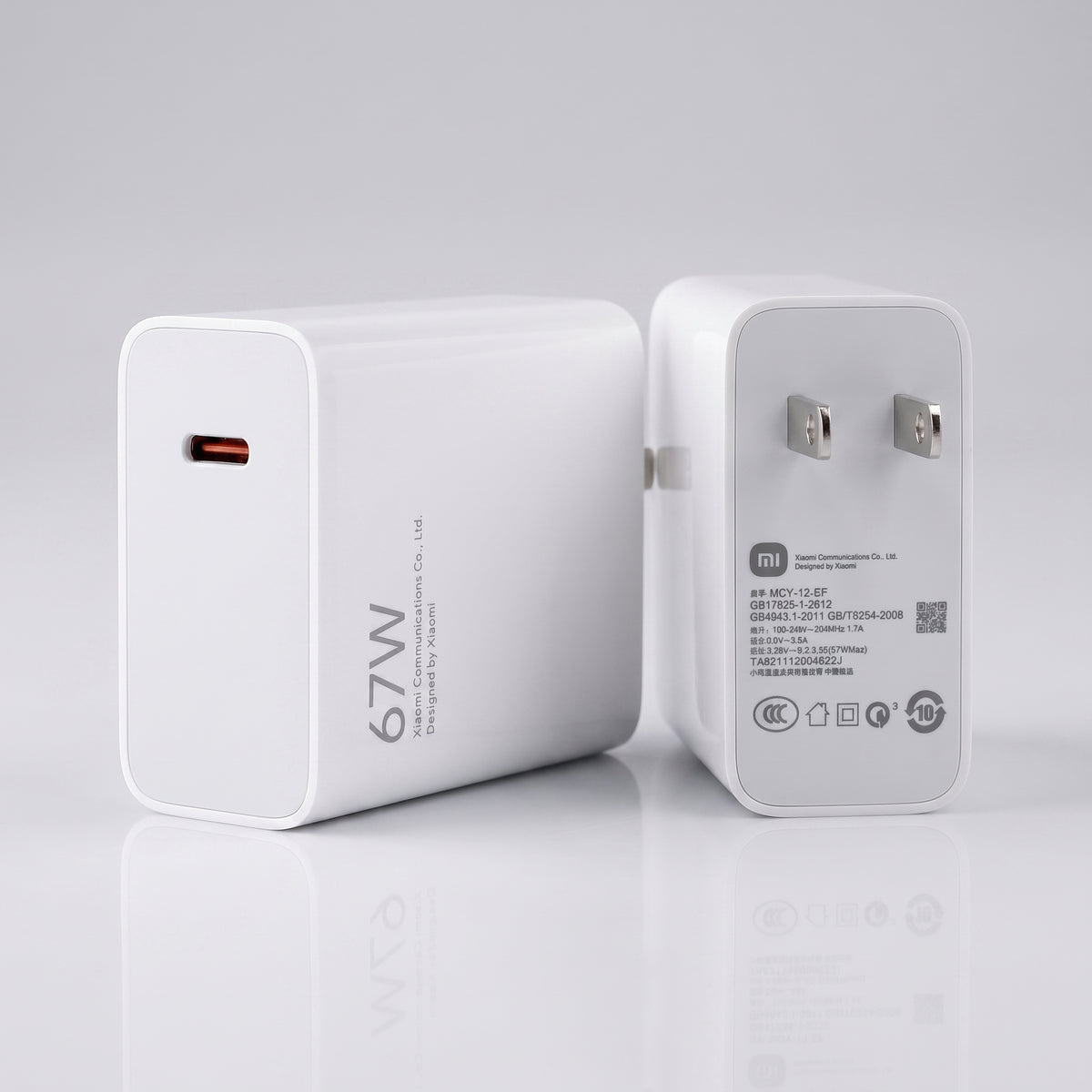 A white 67W USB-C power adapter shown from both the front and back angles on a clean, light gray reflective surface.