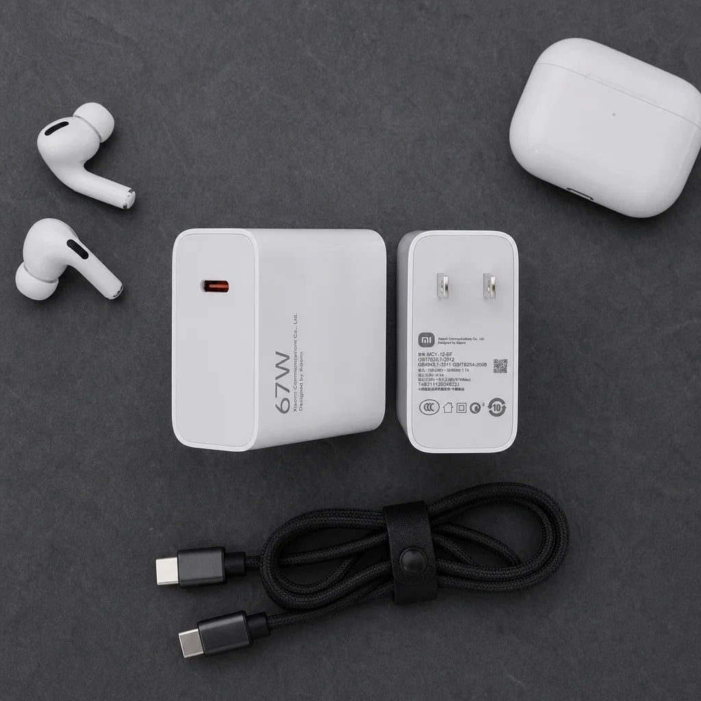 A flat-lay product shot of a white 67W wireless charging setup on a dark gray textured background, including a white wireless earbud charging case, two white wireless earbuds, a white wall charger, a black USB-C to USB-C cable, and a white earbud charging case.
